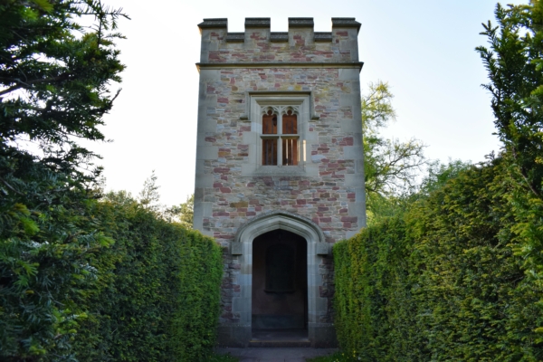 a gothic stone tower, with green hedges either side