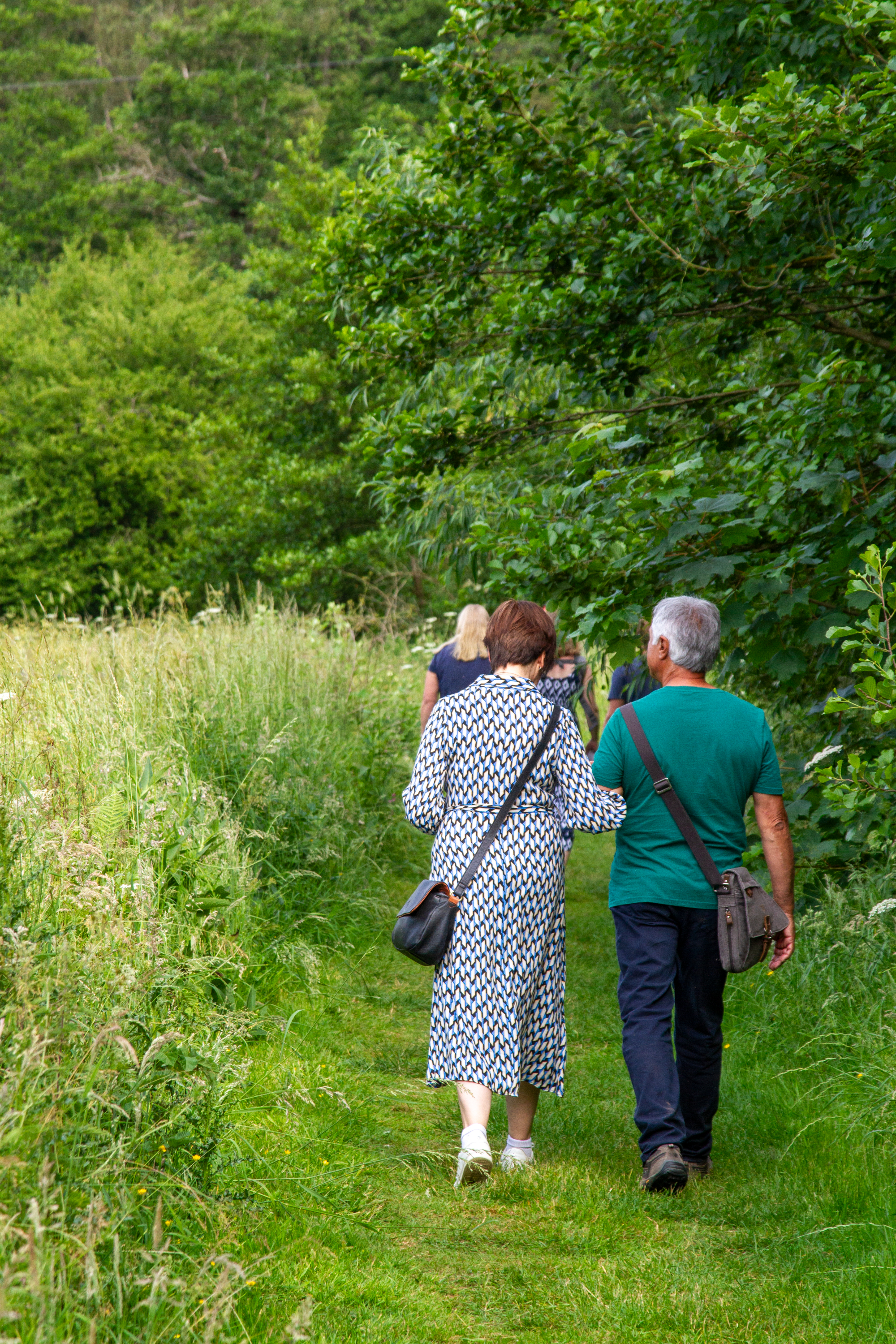 Couple-walk-along-river-walk-surrounded-by-greenery
